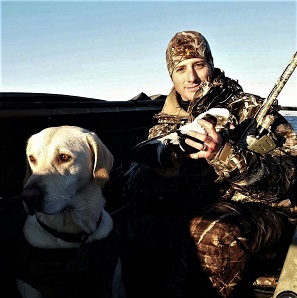 Waterfowl hunter poses with a harvested Long-tailed duck alongside his dog