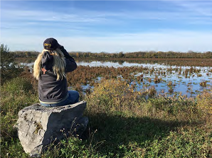 person in a hat and hoodie sits on a rock and observes nature