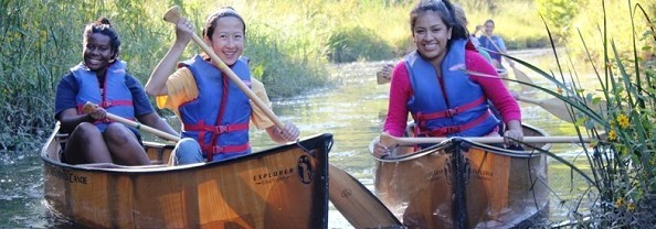 3 young women paddling in canoes.