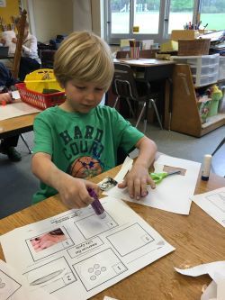 A young students sits at his desk gluing a picture of an eel to a worksheet.