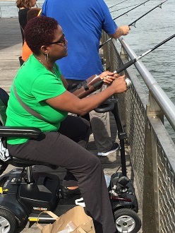 A woman in a wheelchair fishes from a dock.