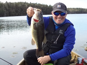 Male angler holding up largemouth bass while wearing life jacket