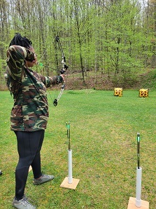 Bowhunting workshop participant practices shooting a target next to a wooded area