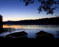 Two canoes sitting on the shoreline of a pond at dusk