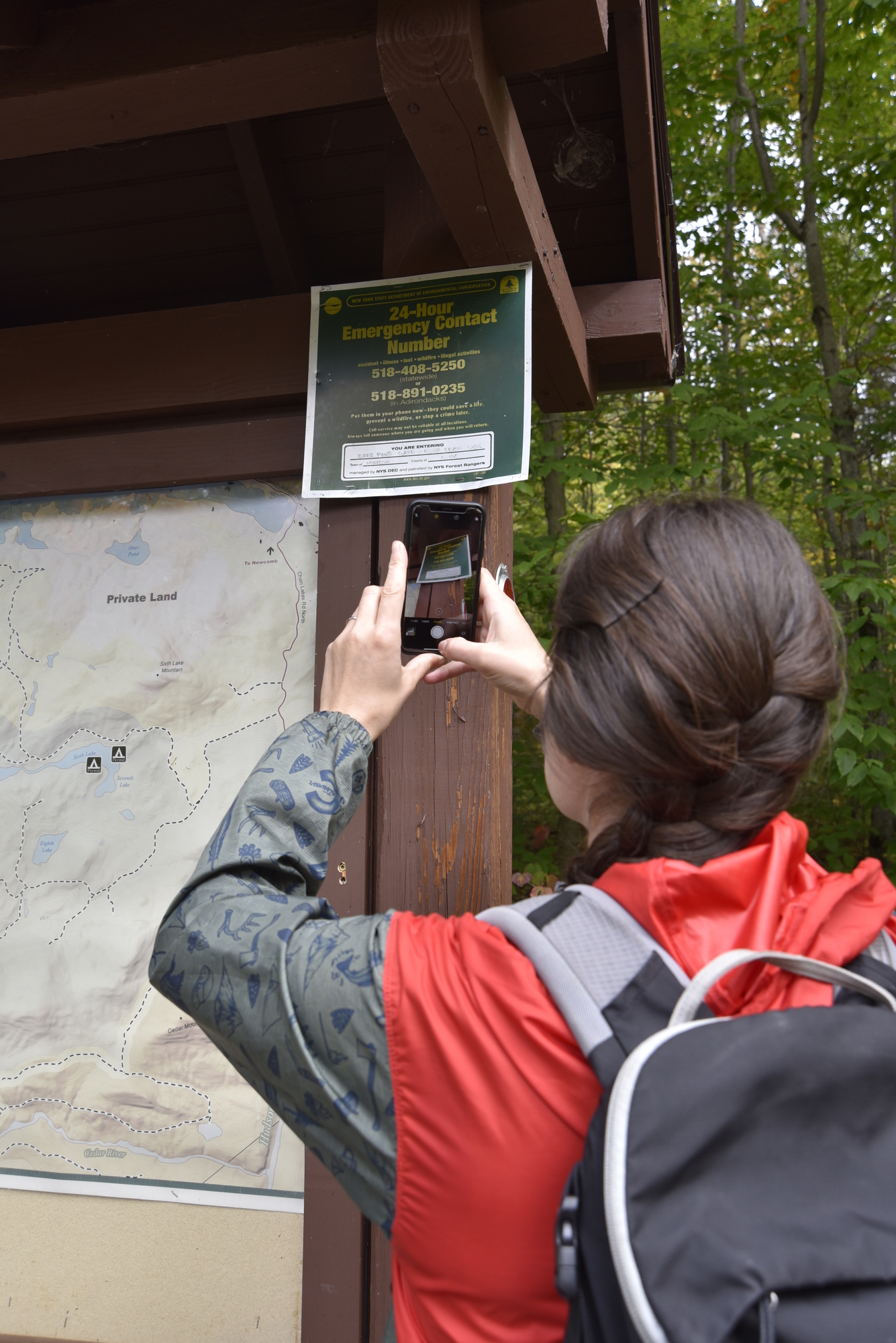Hiker takes photo of emergency contact sign at trailhead