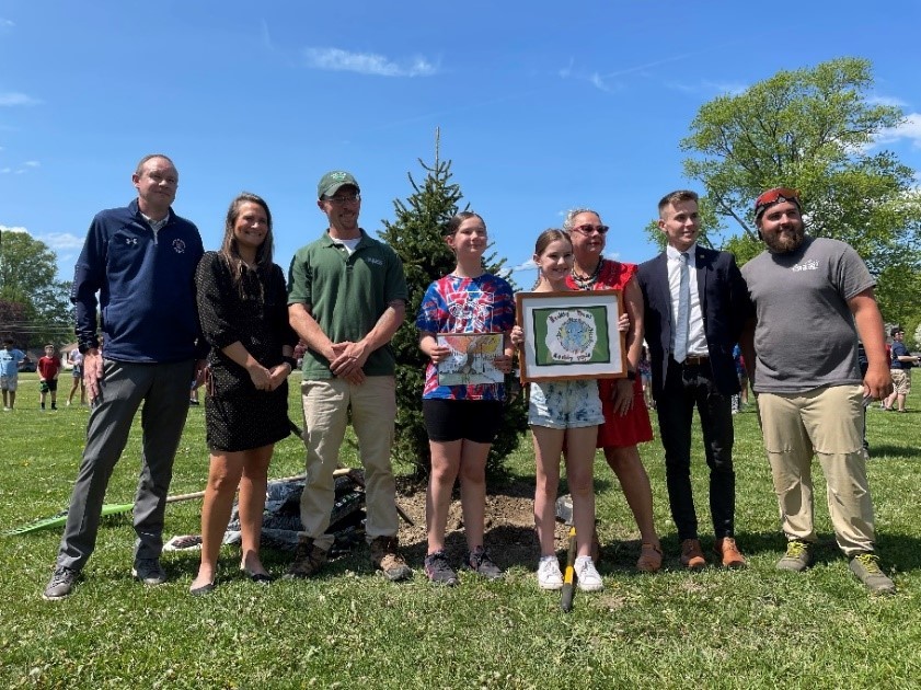 Two winners of 2022 contest with speakers next to the planted tree 