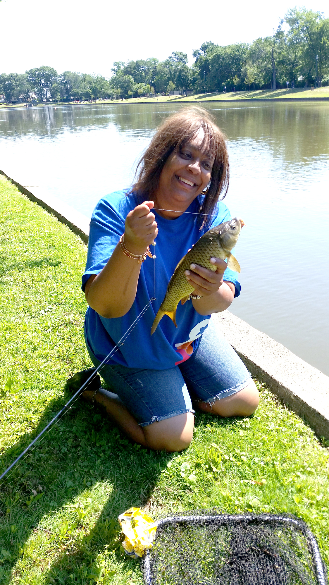 woman next to lake holding carp caught on fishing pole