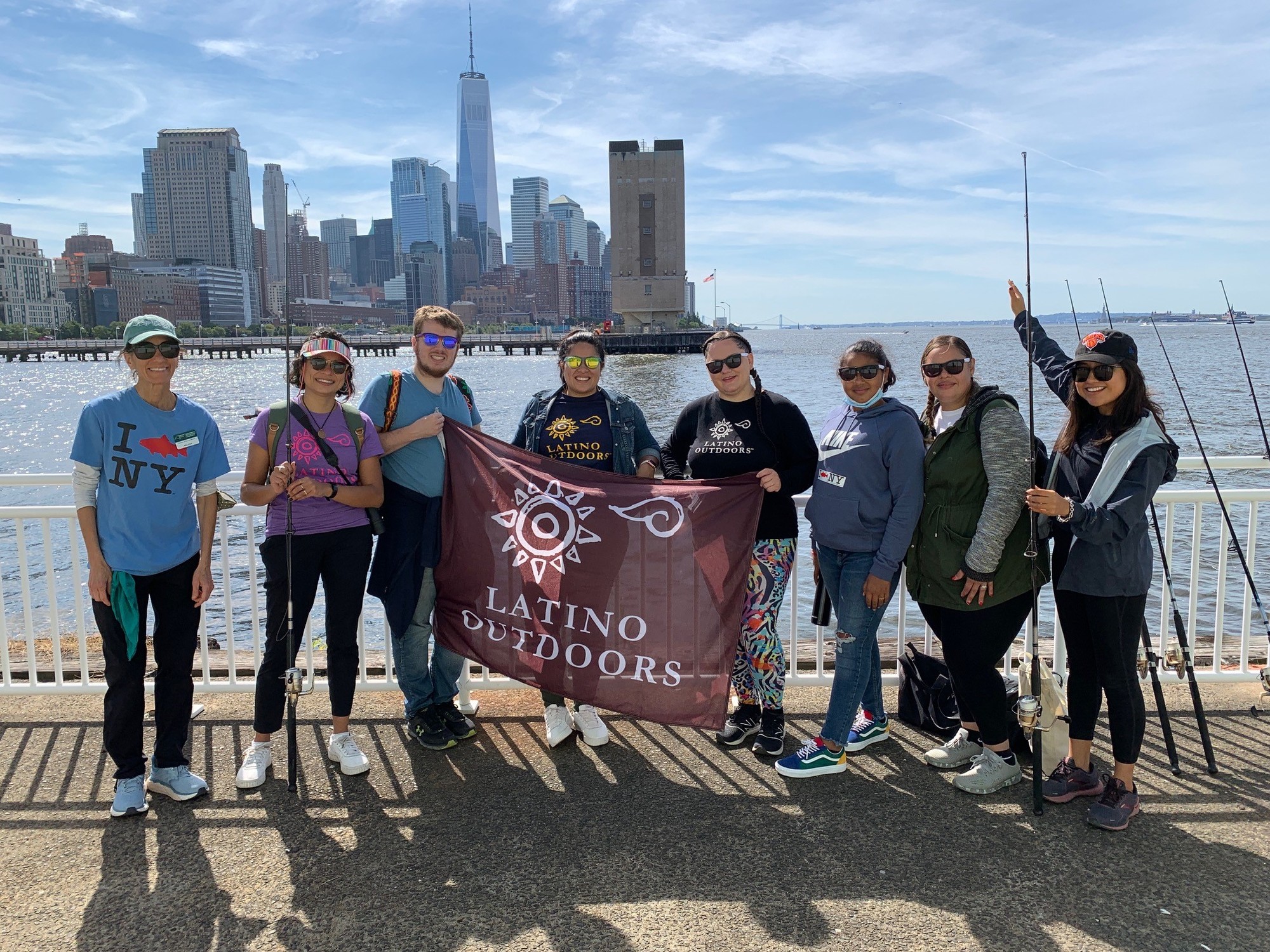 A group of people holding a Latino Outdoors flag standing in front of a NYC back drop