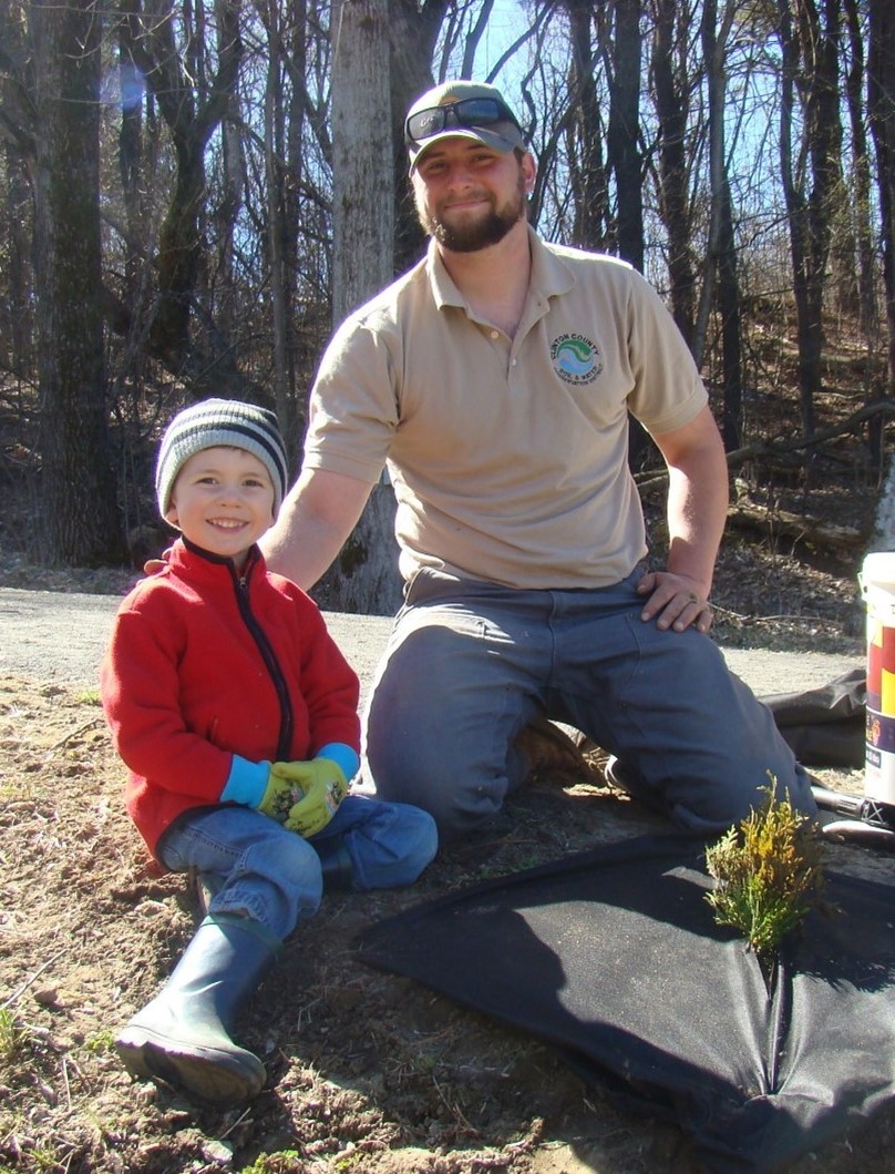 Two tree planters sitting next to a seedling they planted