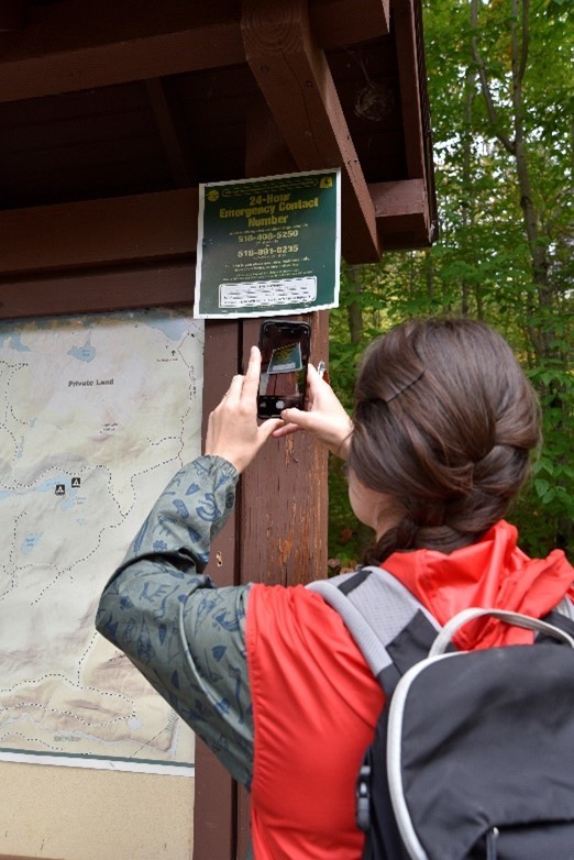A hiker takes a photo of the DEC emergency phone number at the trailhead