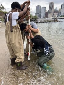 NYC students push a long plastic tube into the sand of the Hudson River.