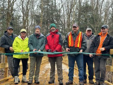 A group of DEC officials holding a green ribbon to cut across Little Sandy Creek Bridge