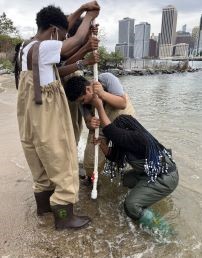 Students stand in water in NYC and look at water in a tube