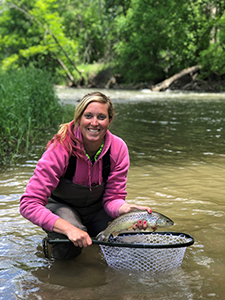 A woman fishing for trout with a net standing in a stream