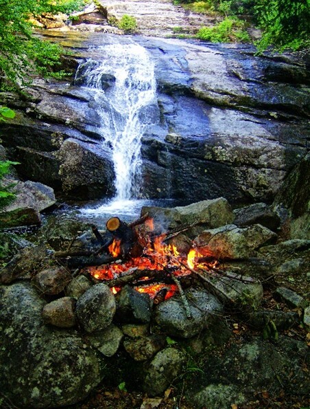 A campfire is lit in front of a waterfall