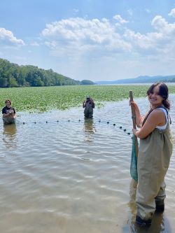 3 young women in waders stand in the Hudson with a seine net.