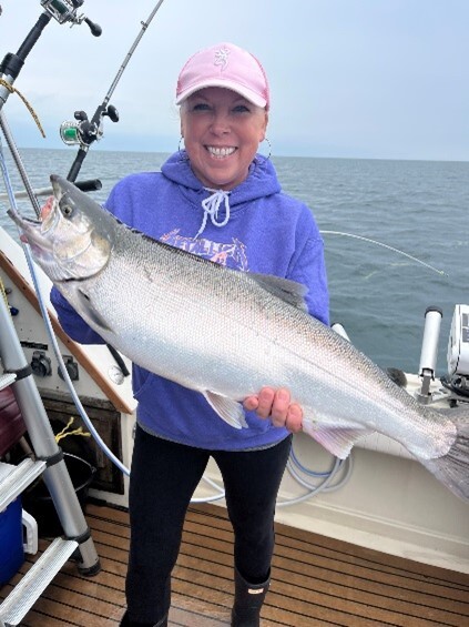 Female angler holding a large Coho salmon on a boat on Lake Ontario.