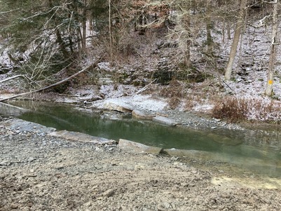 Large stone cross vanes, creating a pool of water in the West Branch Owego Creek near a fishing access site with a light coating of snow.