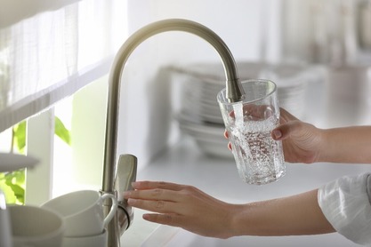 An individual filling a glass with water from a faucet. 
