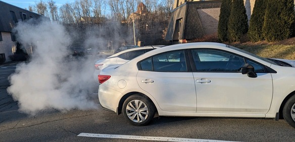 A car idling in a parking spot with emissions coming from the exhaust.