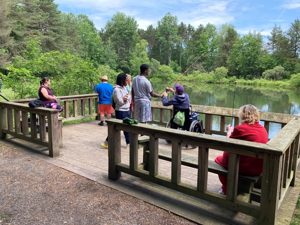 A group of people sit on an accessible dock and are learning to fish. 