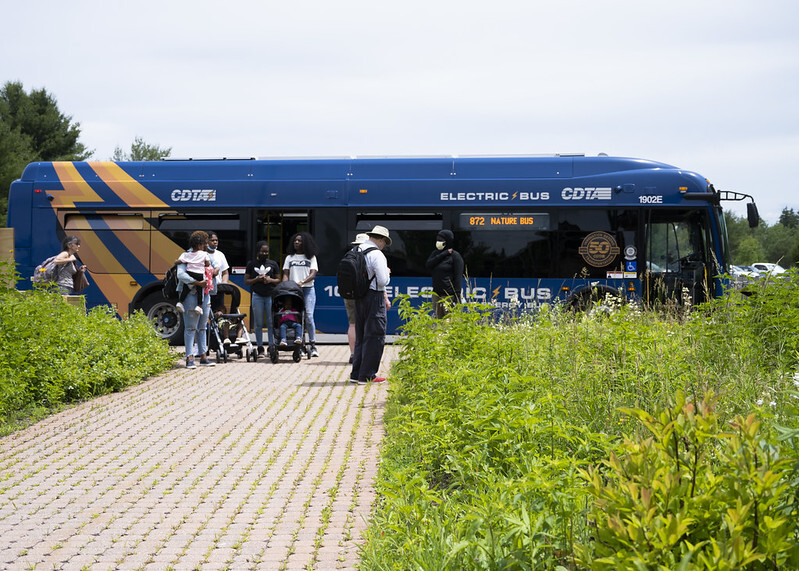 A group of people stand in front of the CDTA Electric Nature Bus. 