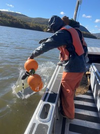 A man on a boat lowers an acoustic receiver into the Hudson