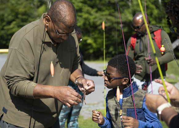 An adult teaches a child how to bait the hook of their fishing pole. 