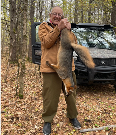 A man stands holding a successfully harvested gray fox in front of him