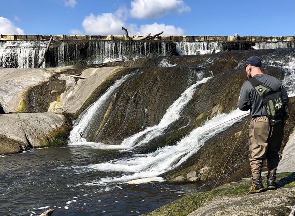 Angler in waders fishing off rocks near a waterfall