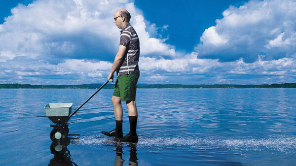 Image of a man with fertilizer spreader walking and spreading on a body of water