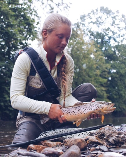 Angler holding a trout along the bank of a stream