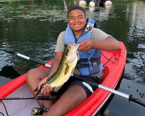 angler holding largemouth bass up while sitting in a kayak on a waterbody