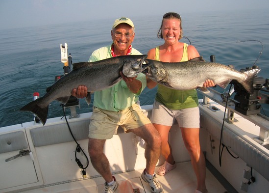 Anglers holding up salmon caught off boat in a lake
