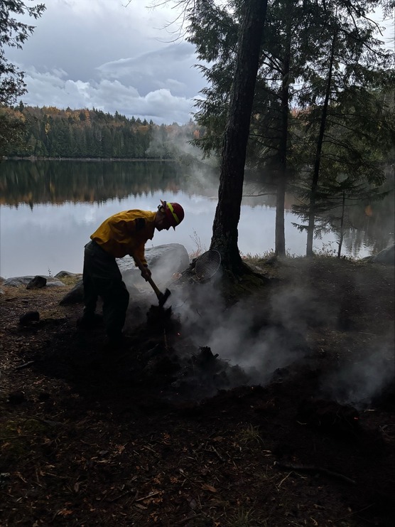 Ranger using axe to dig a ditch near smokey fire remains