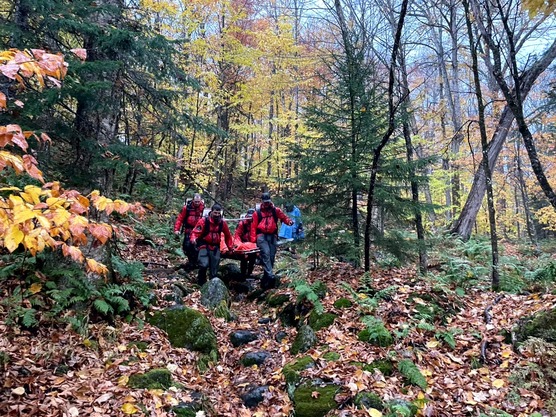 Rangers carrying injured hiker down rocky, wooded trail