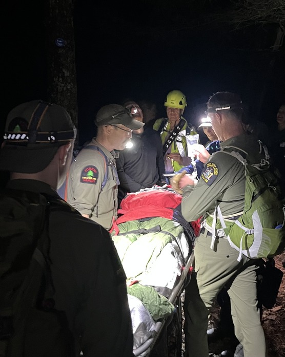 Rangers carry out injured hiker down a dark wooded trail