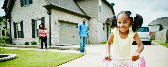 A family with children playing outside their home with car in the driveway.