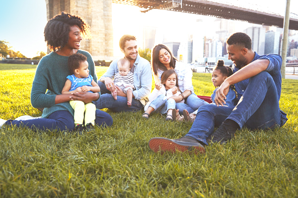 Two couples with children sitting on grass with Brooklyn bridge in the background