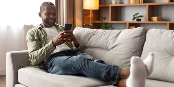 Man laying on couch filing taxes on his phone