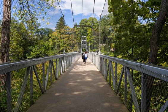 A person in the distance walking across a pedestrian suspension bridge in a lush green forest