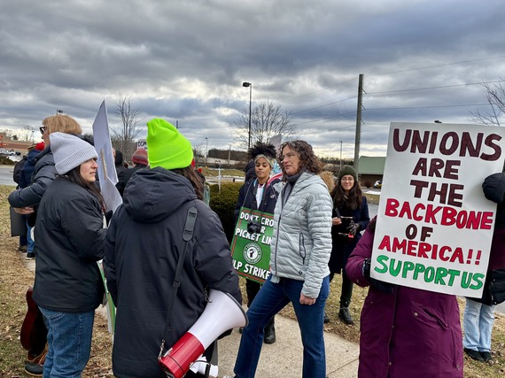 Executive Metzger talks to striking Starbucks workers at the picket line. In the foreground, a poster reads "Unions are the backbone of America!!"