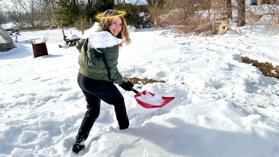 A young student shoveling snow with angel wings and a halo