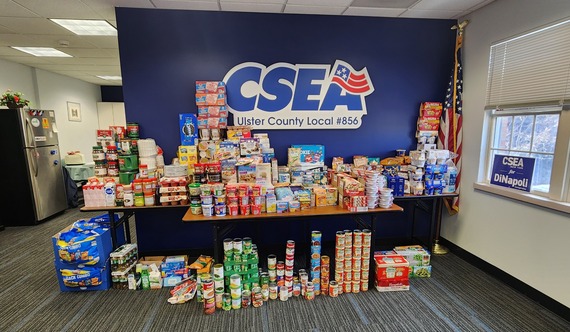A pile of donated food in front of the CSEA logo on a wall