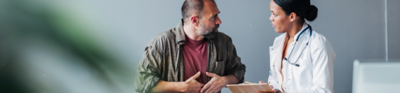 A doctor taking notes on a clipboard while a patient describes their symptoms.
