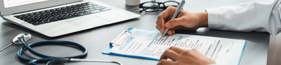 A medical professional filling out a form and working on a laptop.