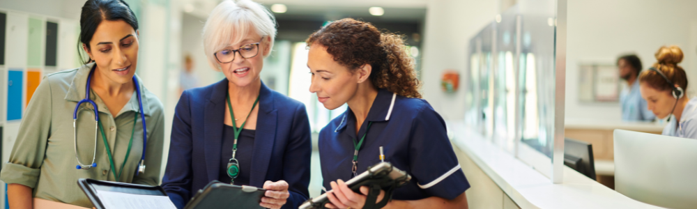 Three healthcare professionals review information together on a tablet in a clinical setting
