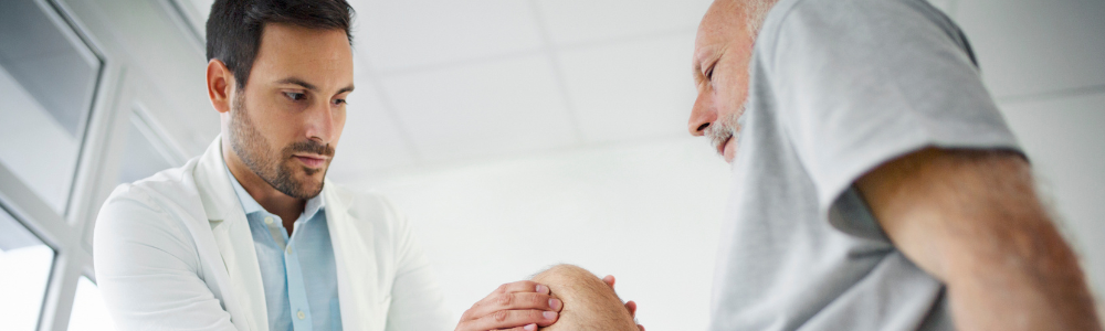 A healthcare professional examines a patient's knee in a bright clinical room.