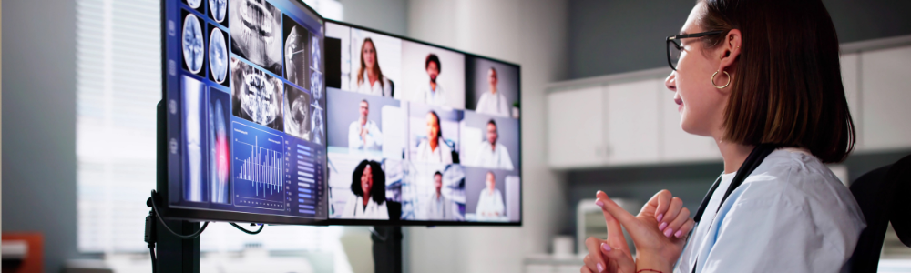 Healthcare worker joins a virtual meeting, viewing medical images and multiple professionals on a large screen.