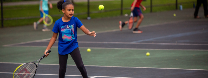 Little girl serving tennis ball holding tennis racket 